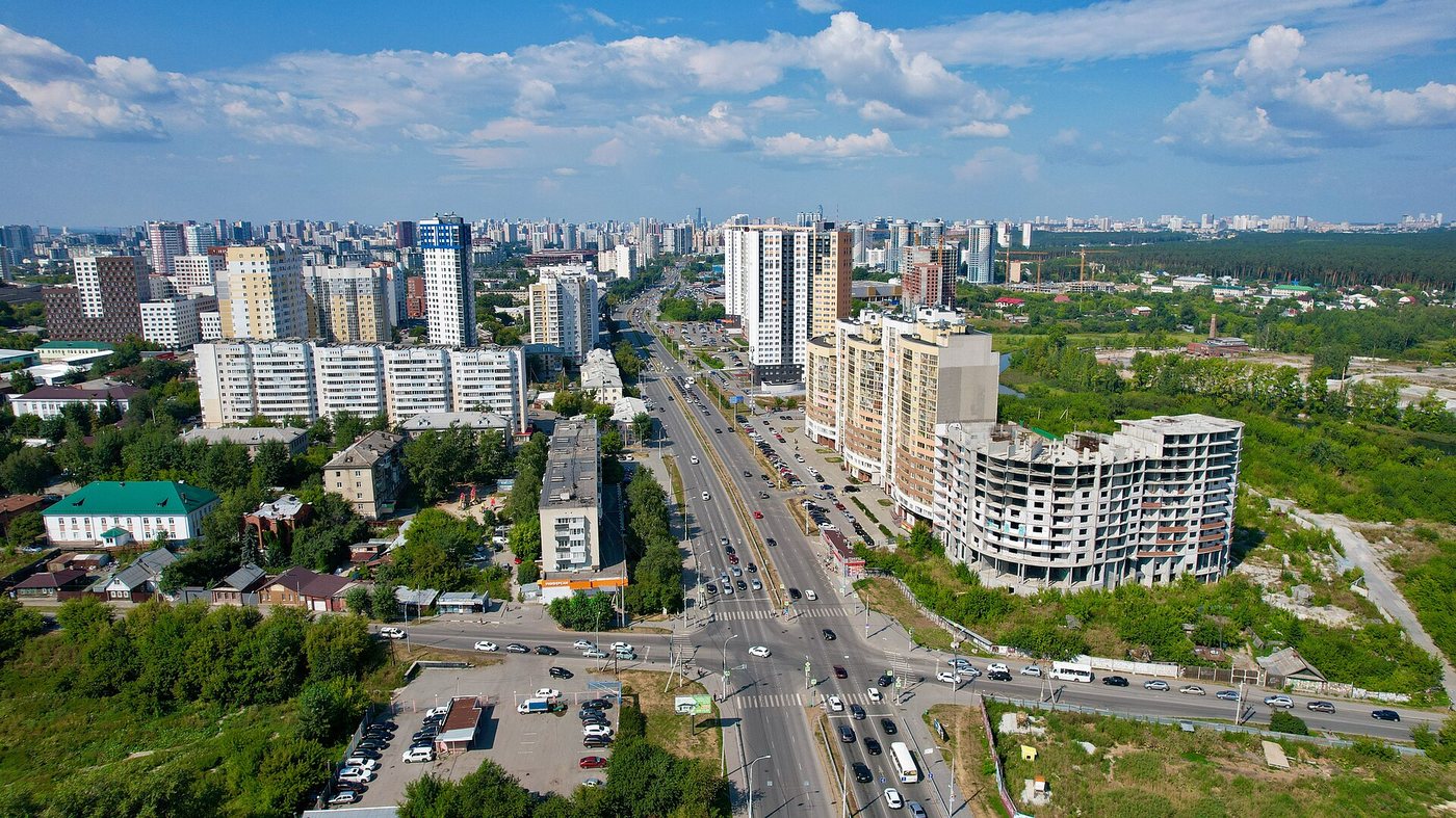 Долгострой на ул. Щербакова, 20 у перекрёстка с ул. Лыжников (справа серый каркас недостроенных секций рядом со сданными очередями) — его СК «Союз» выкупила и с 2026 года достраивает. Снимок с высоты, 20 августа 2022 года.